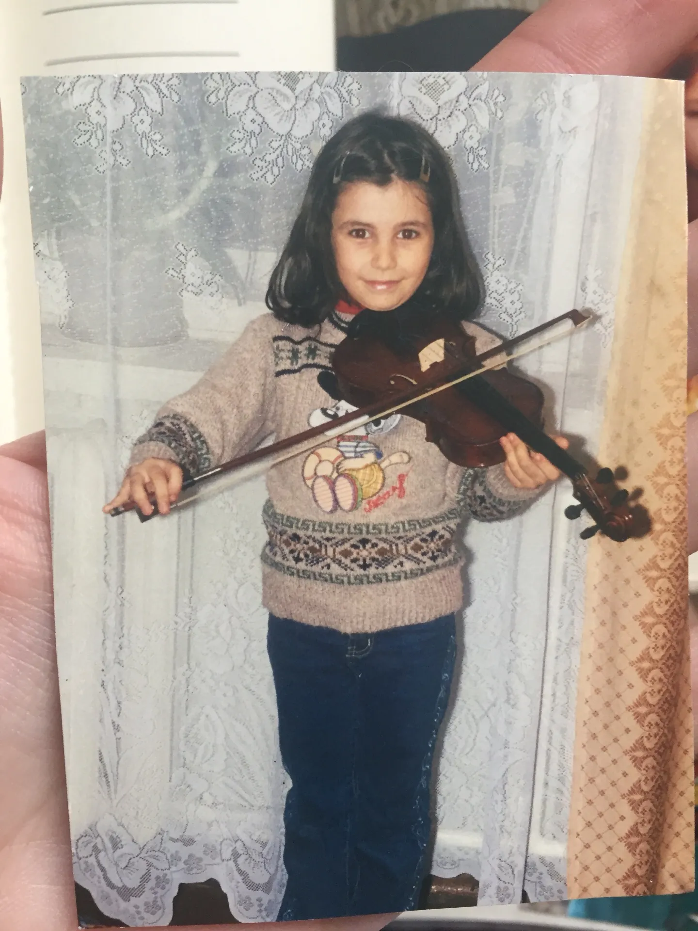 Tatev Muradyan giving a home concert at the age of 7, smiling and holding a violin.